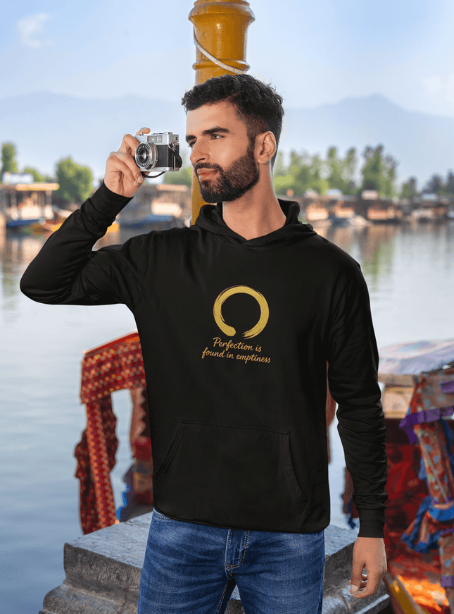 Mann im Perfection Herren Hoodie mit goldenem Enso-Symbol, fotografiert in malerischer Hafenstadt.